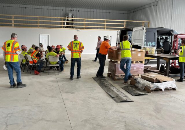 Barrett Midwest Division team in safety vests gathers indoors, discussing Earth Day projects for Barrett Paving.