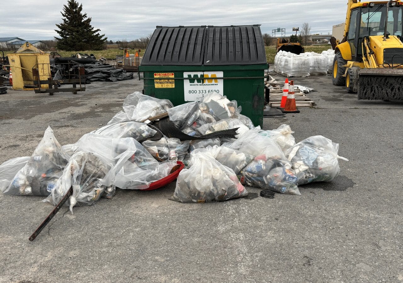 Bags of collected trash by a dumpster during Barrett Paving’s Earth Day cleanup in New York's northeast division.